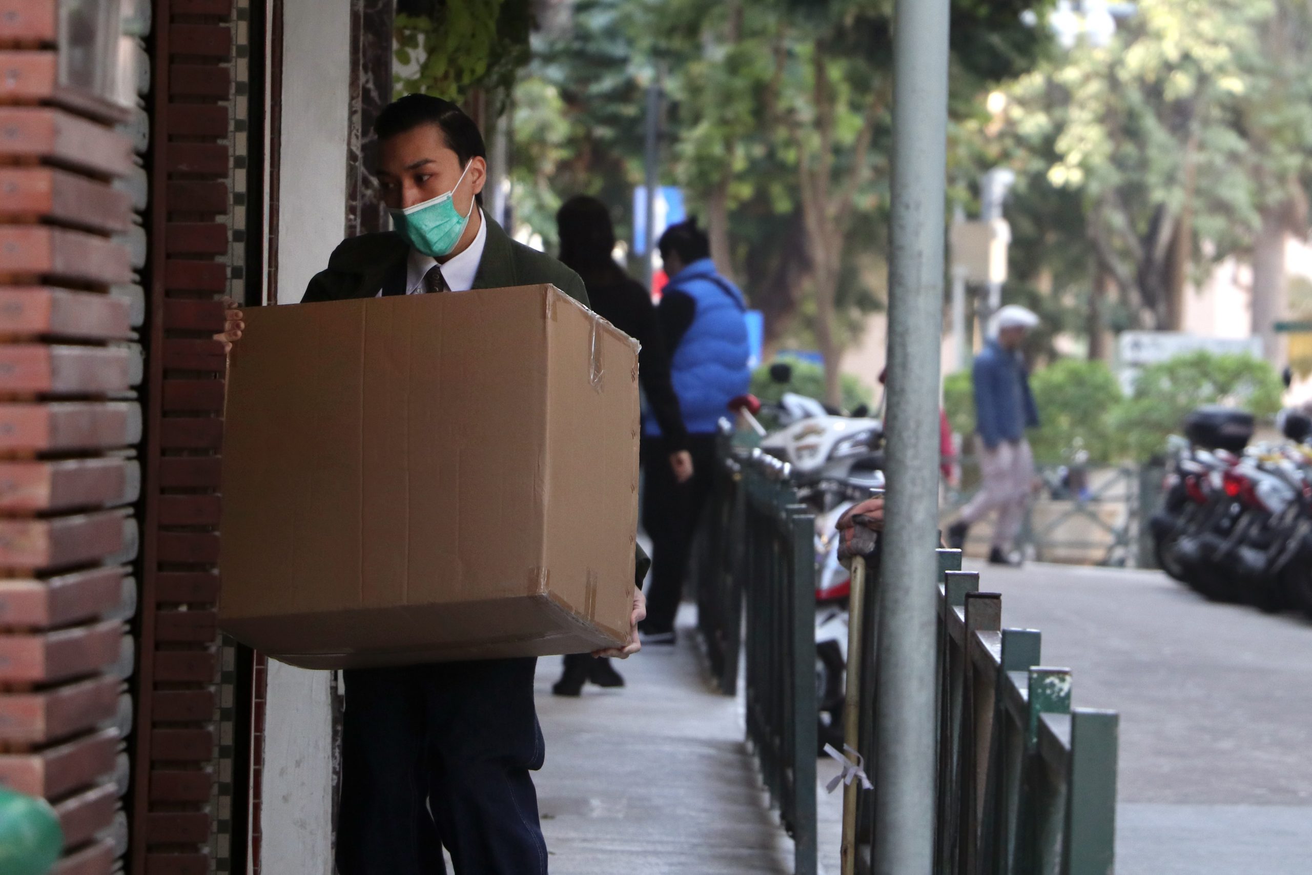 man in black jacket carrying brown cardboard box to protect from coronavirus